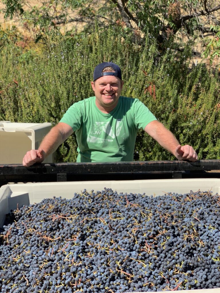 Daniel with arms on side of trailer looking at freshly harvested VINCENT VINES Estate Merlot