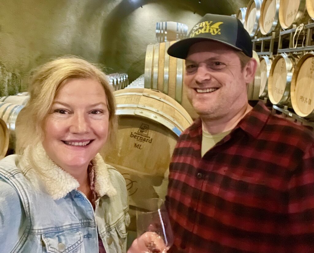 Aubrey and Daniel smiling in front of wine barrels in the barrel cave