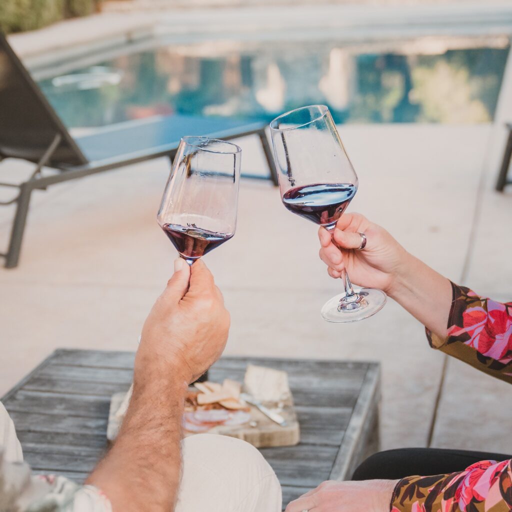 Couple toasting with VINCENT VINES Estate Merlot during a wine experience by the pool at Vineyard Chateau